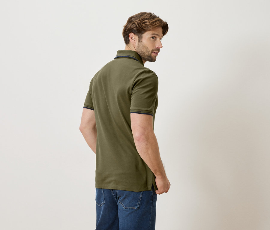 Homme vu de dos portant un polo vert olive et un jean sur un fond clair.