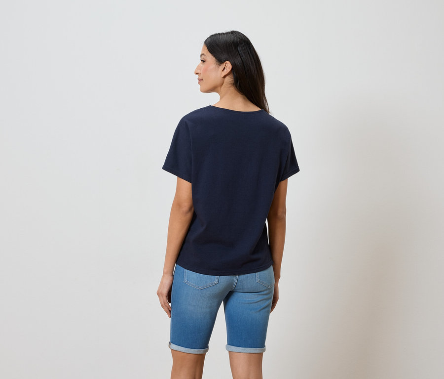 Vue de dos d'une femme aux cheveux foncés portant un t-shirt bleu marine et un short en jean.