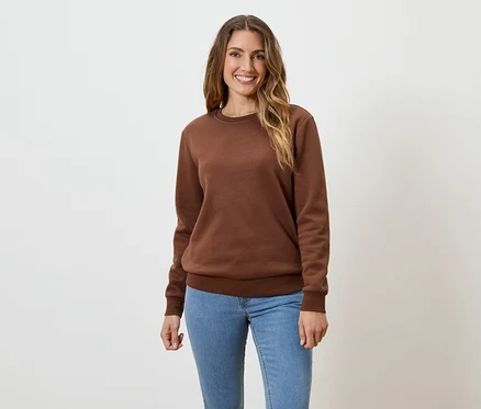 Une femme aux longs cheveux bruns ondulés porte un sweat-shirt marron et un jean sur un fond blanc.
