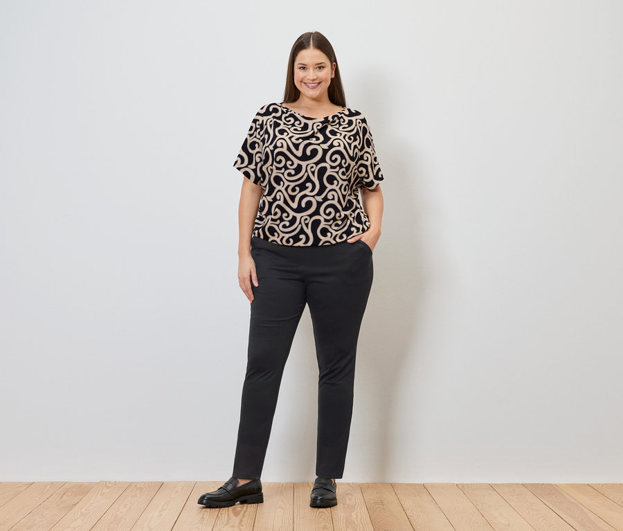 Femme portant un haut à motifs et un pantalon de jogging, une main dans la poche.