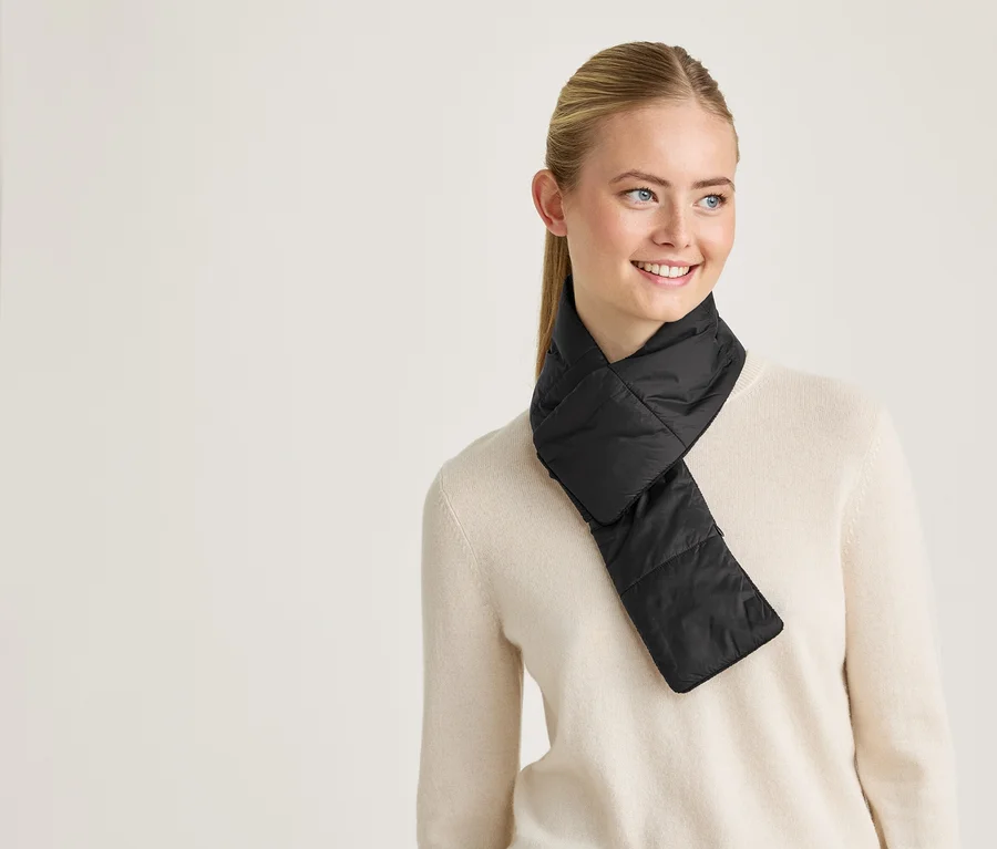 Une femme blonde portant un pull beige porte une écharpe noire matelassée.