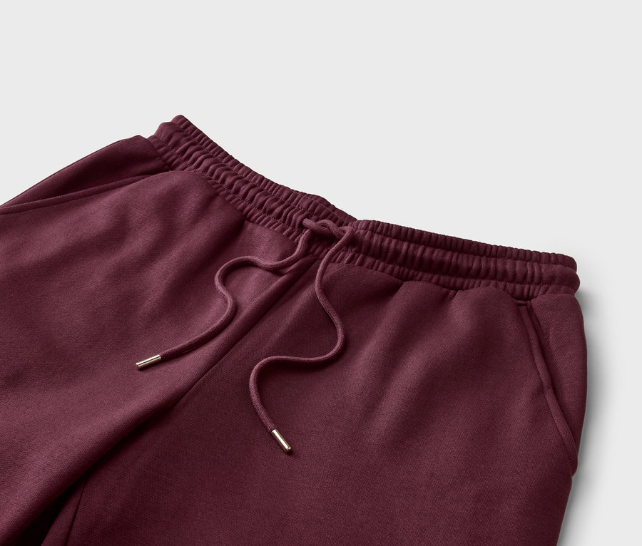 Gros plan d'un pantalon de jogging bordeaux avec cordon de serrage et taille élastique sur fond gris clair.