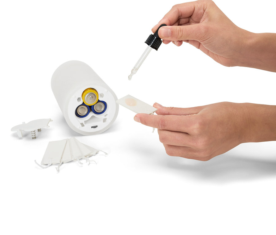 Une main verse du liquide d'une pipette sur un diffuseur de parfum blanc fonctionnant sur piles.