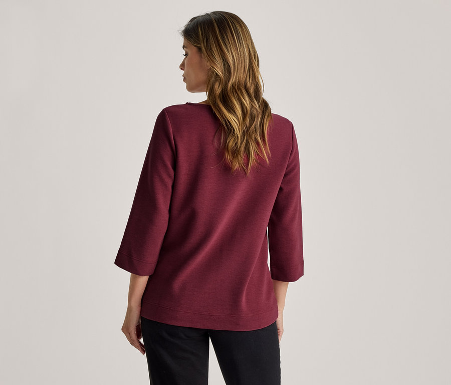 Femme vue de dos, portant un haut bordeaux à manches trois quarts et un pantalon noir.