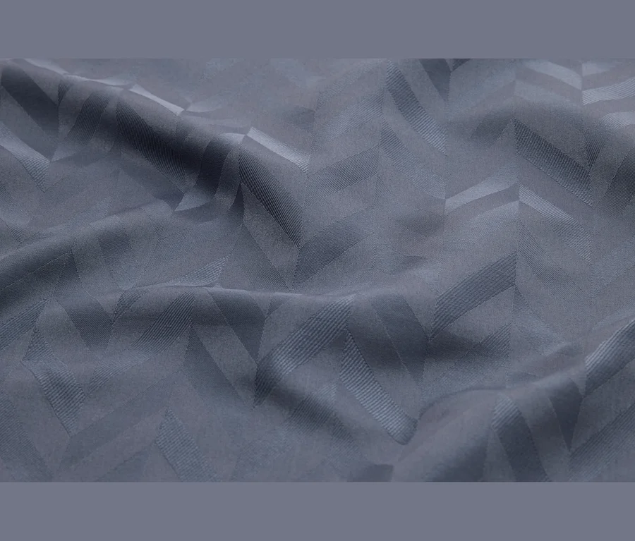 Tissu gris drapé avec un motif chevron subtil et tissé, visible par les variations de texture et de lumière.