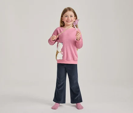 Fille souriante aux cheveux longs portant un sweat-shirt rose avec un ours polaire à paillettes, un pantalon large bleu foncé et des chaussettes roses, tenant une baguette étoile rose.