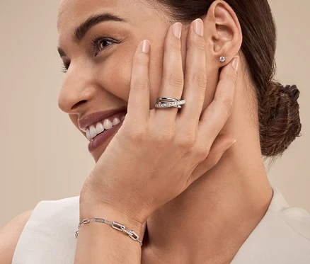 Une femme avec une bague et un bracelet en argent sourit et regarde vers la gauche.
