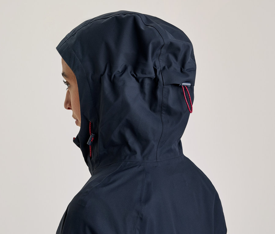 Personne de profil portant une veste à capuche bleu foncé, avec la capuche relevée et des cordons rouges.