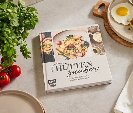 Sur une table, il y a un livre de cuisine, une assiette de nourriture, un œuf, un verre de tomates, du persil et des tomates.