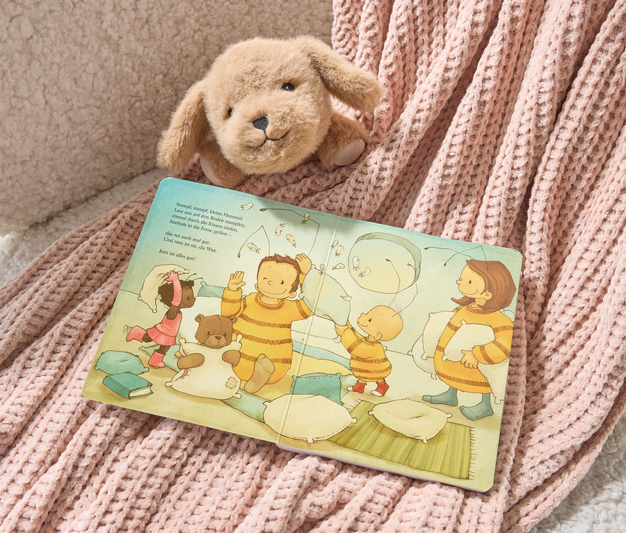 Un chien en peluche est posé sur le livre « Bébé Bourdon Bommel » (en allemand) et une couverture tricotée rose.