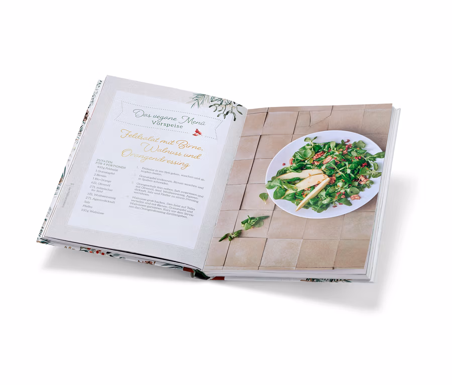Livre de cuisine ouvert « Christmas is a feeling » avec une recette de salade de mâche aux poires et à la vinaigrette aux noix et une assiette de salade finie.