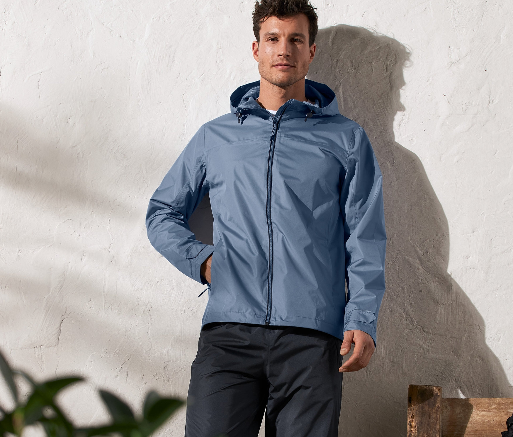 Un homme debout portant une veste de pluie unisexe bleue.