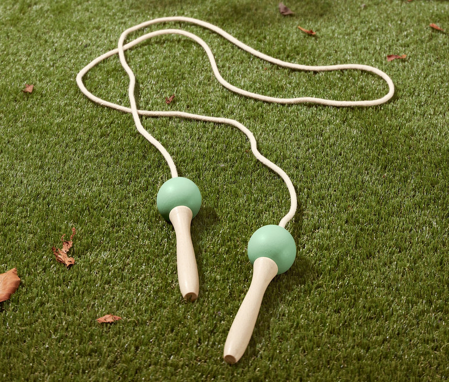 Une corde à sauter blanche avec des poignées vertes sur l'herbe.