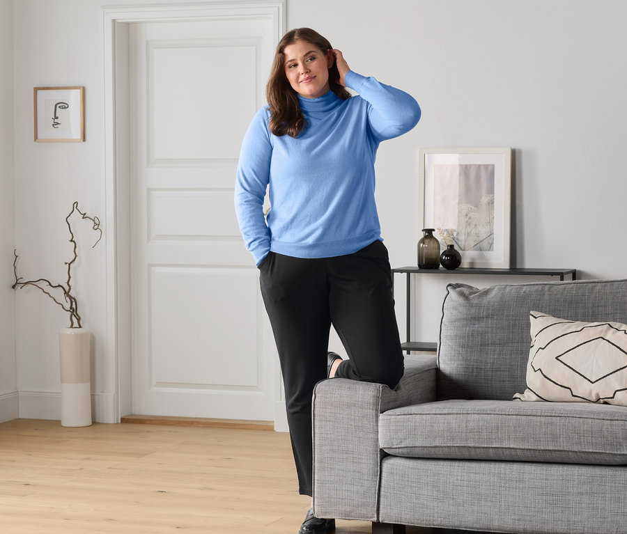 Femme posant dans un pull en maille bleu clair avec col montant et un pantalon de jogging à carreaux.