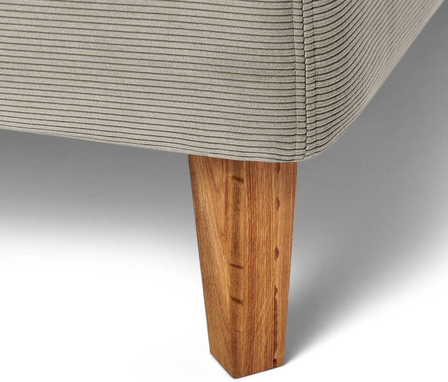 Gros plan sur un lit à sommier tapissier beige avec un pied en bois.