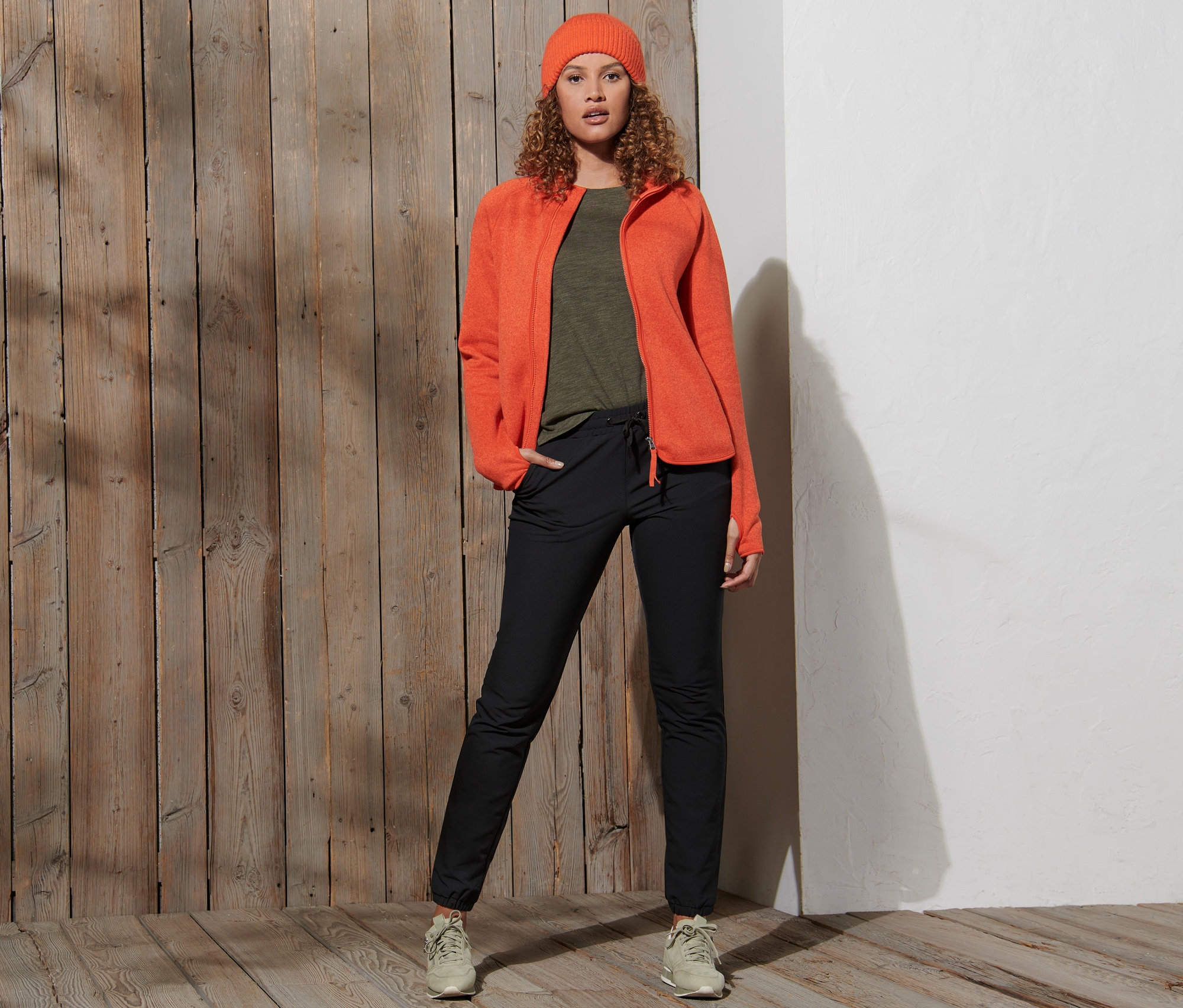 Femme posant en veste orange et pantalon de jogging softshell noir.