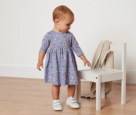 Un bébé debout porte une robe en jersey à motif floral.