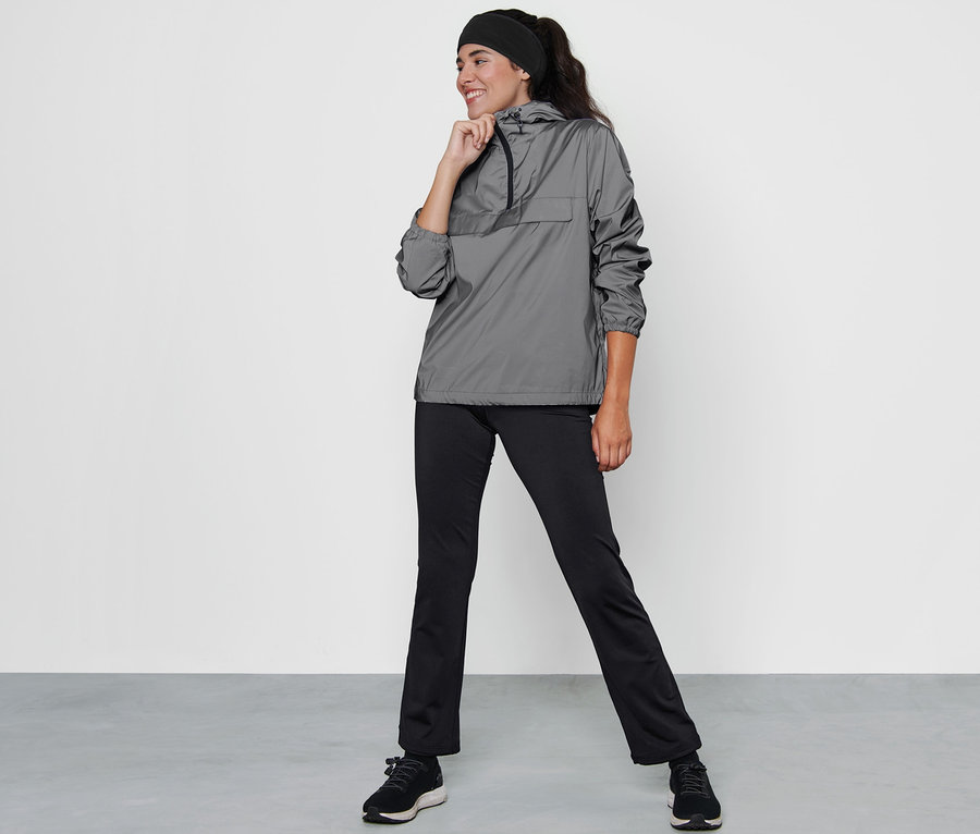 Femme posant en veste coupe-vent réfléchissante grise, pantalon noir et chaussures.