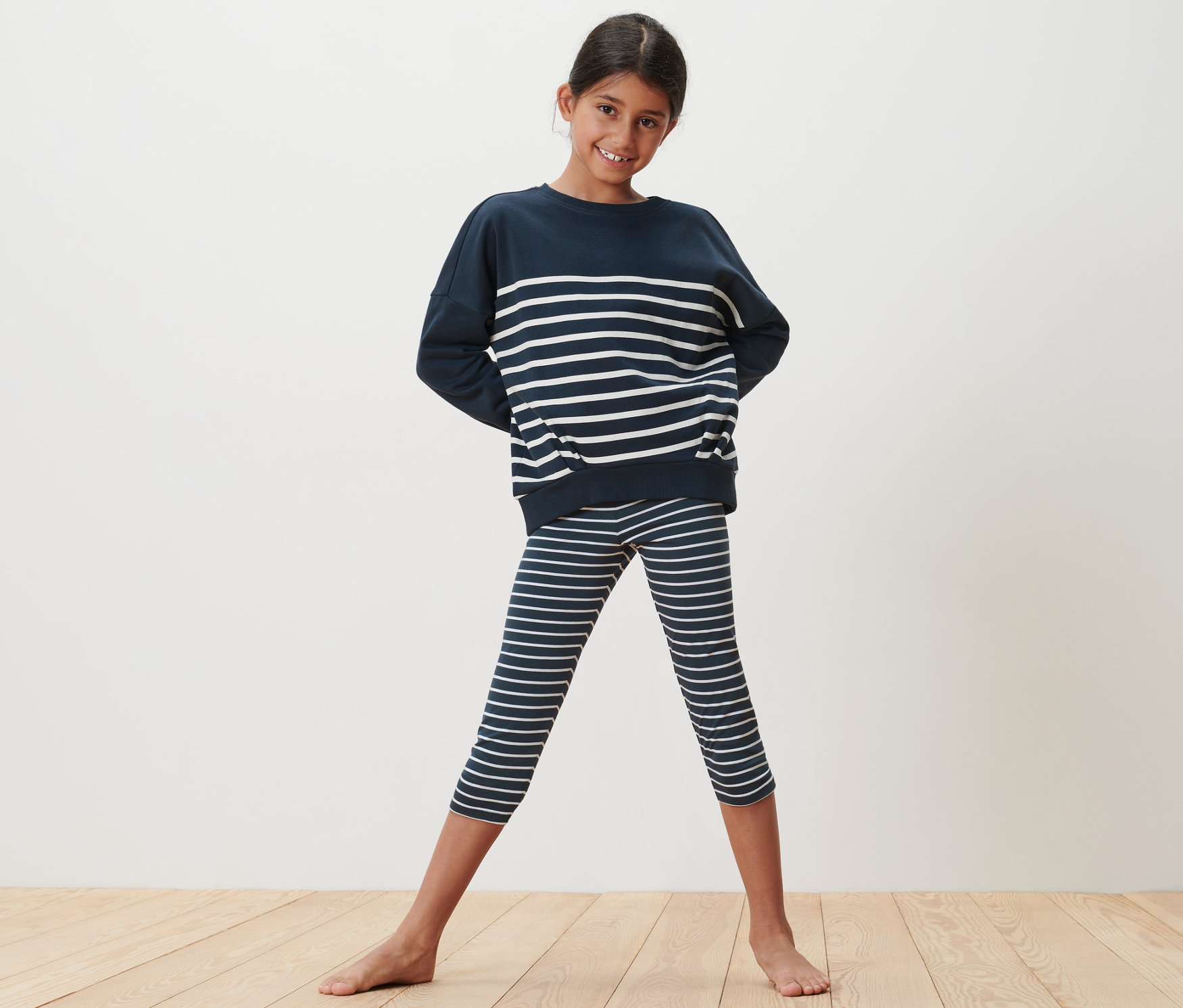 Une fille souriante pose dans un ensemble rayé marine composé d'un legging 3/4 et d'un pull.