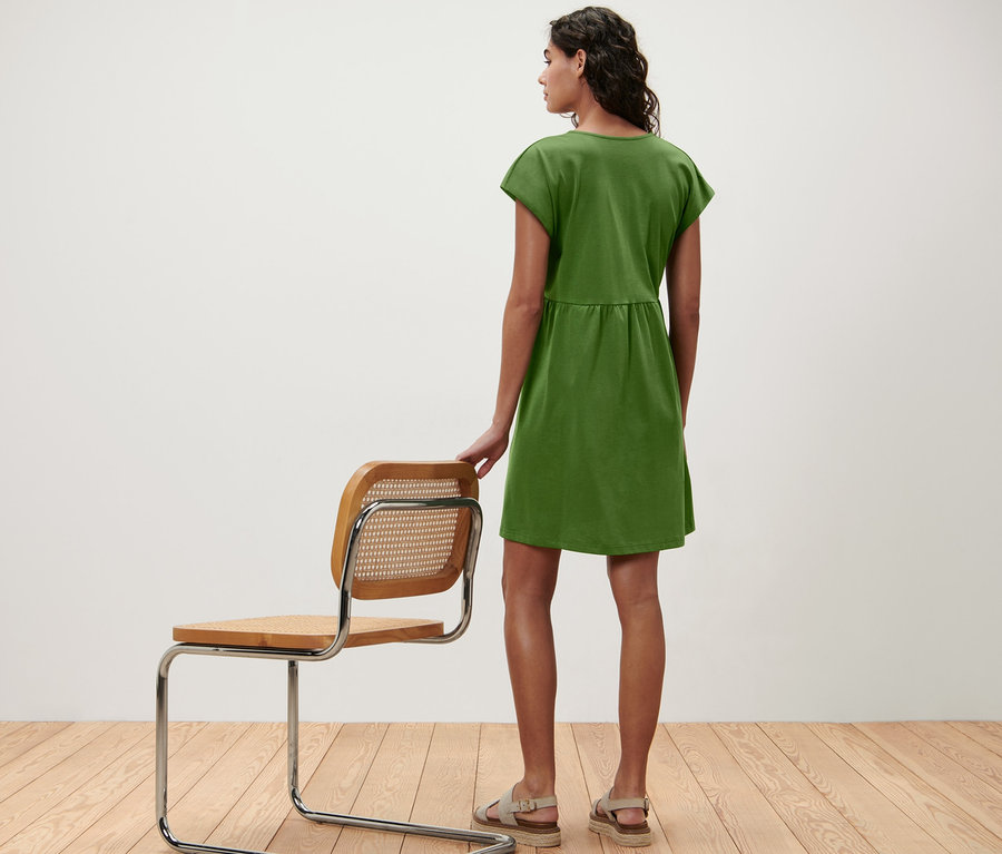 Une femme vue de dos porte une robe en jersey et pose sa main sur une chaise.