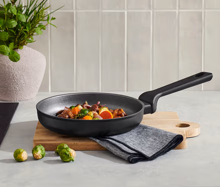 Sur un comptoir de cuisine, une poêle en aluminium de qualité professionnelle d'environ 20 cm contenant des aliments et trois choux de Bruxelles.