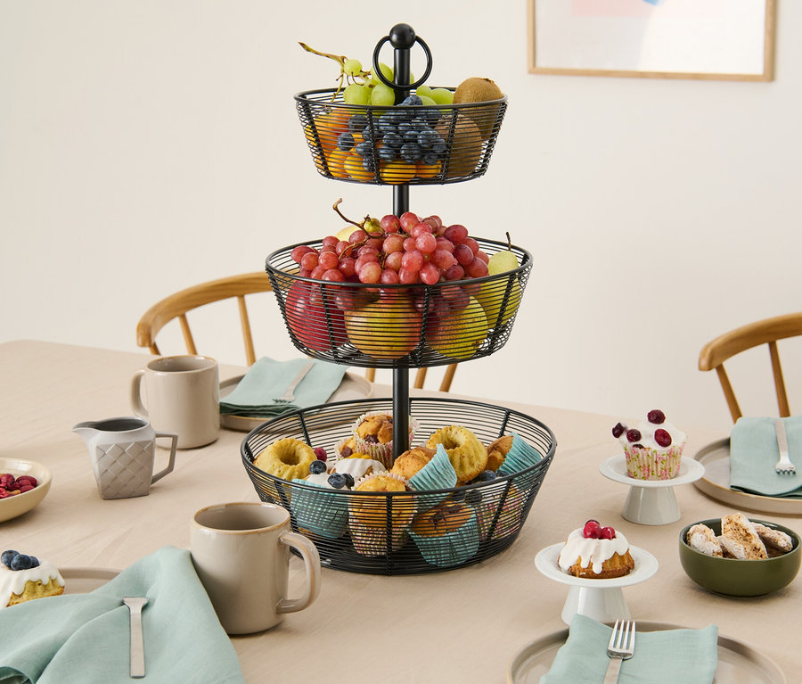 Un plateau à trois étages avec des fruits et des muffins est posé sur une table.