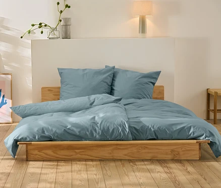 Parure de lit en percale bleue de taille standard et grande taille sur un lit en bois.