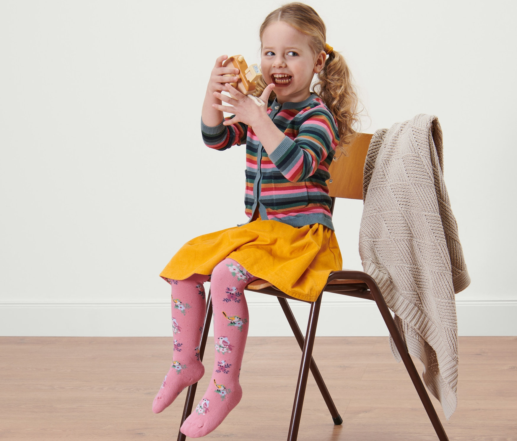 Une fille est assise sur une chaise et mange un beignet. Elle porte une jupe jaune et 5 collants en coton rose pour enfant.
