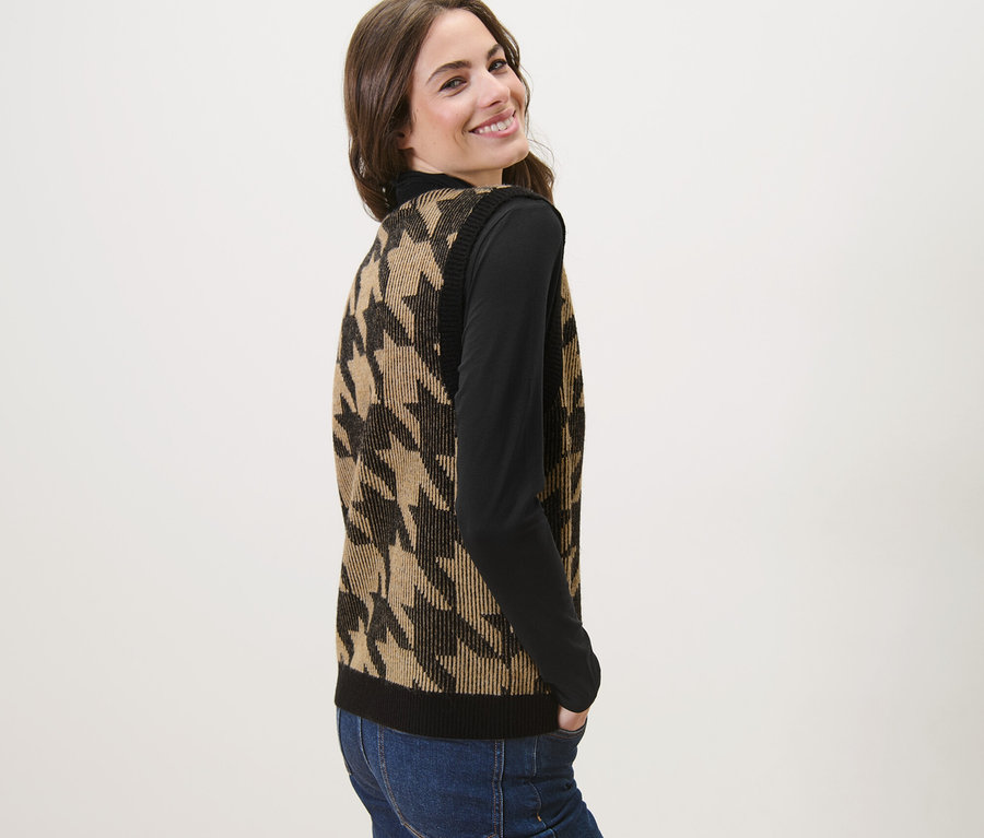 Une femme souriant par-dessus son épaule porte une veste sans manches en maille à jacquard pied-de-poule.