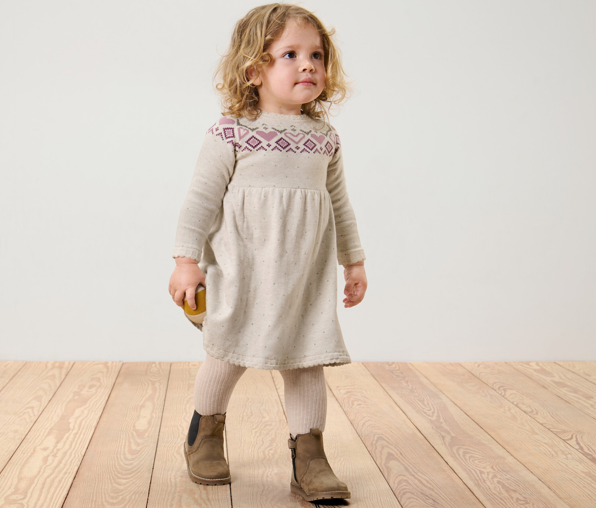 Une fille se tient sur un plancher en bois et porte une robe en maille pour enfant.