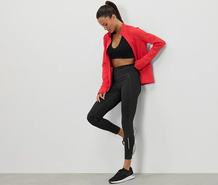 Femme posant en legging de sport noir et veste rouge.