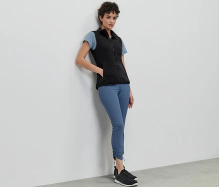 Une femme appuyée contre un mur porte un gilet sans manches en polaire, un t-shirt et un legging.