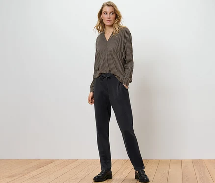 Femme blonde debout portant un pantalon de jogging et un chemisier à motifs.