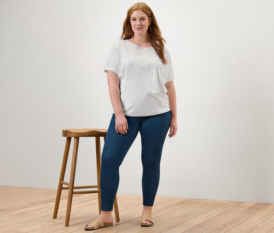 Une femme debout portant une blouse blanche à broderie et un jegging.