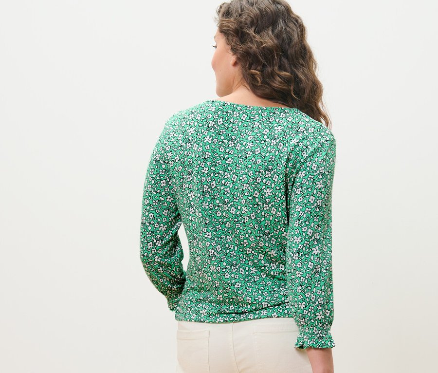 Femme vue de dos portant une blouse imprimée verte.