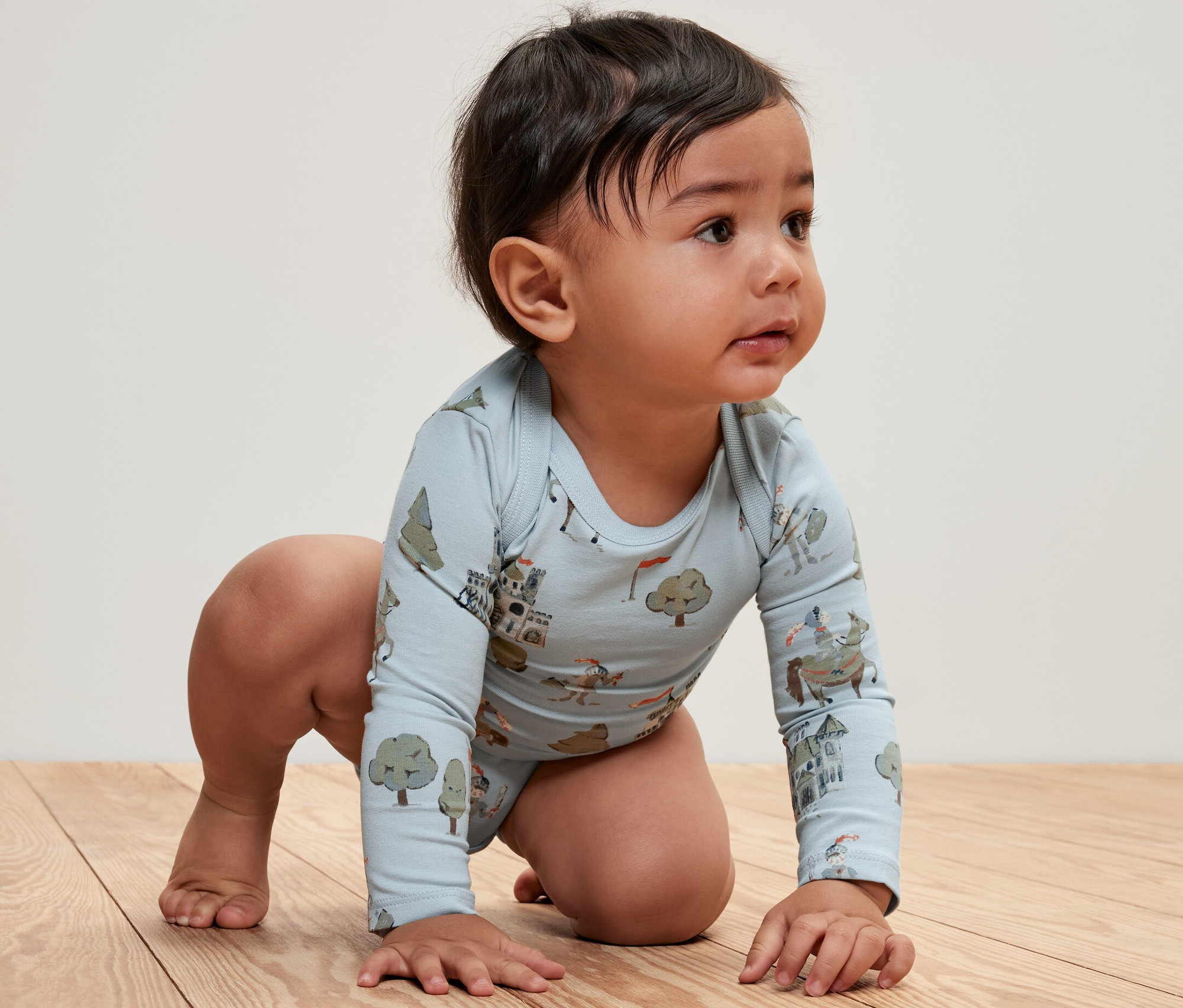 Un bébé à quatre pattes sur un plancher en bois, portant un body bébé bleu clair à motif de chevalier (lot de 5).