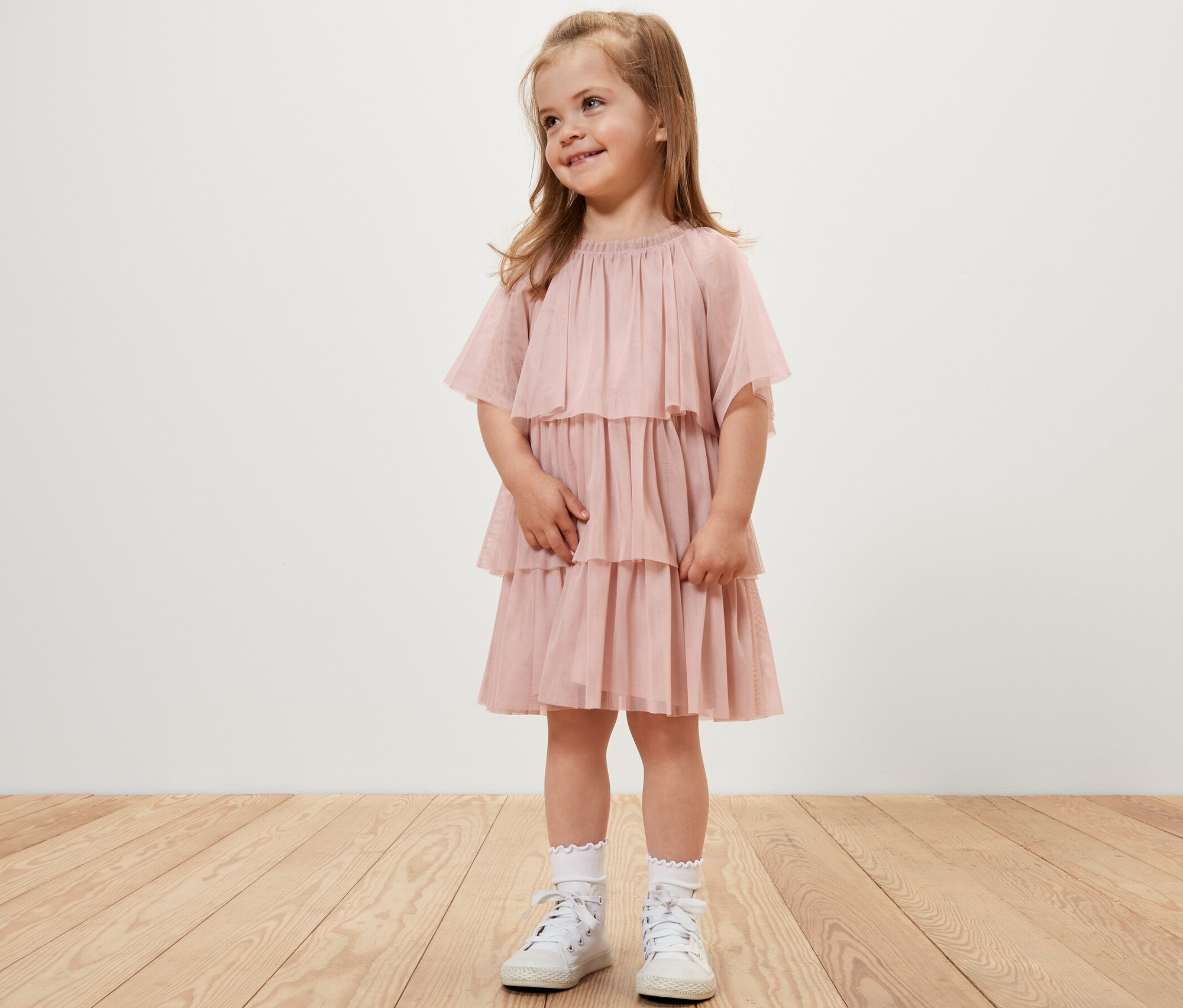 Une fillette souriante porte une robe en tulle pour enfant.