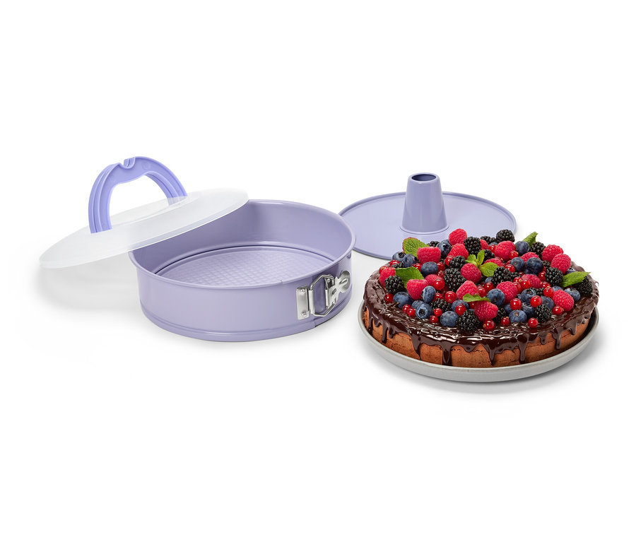 Moule à charnière violet avec couvercle de transport à côté d'un gâteau au chocolat et aux fruits.