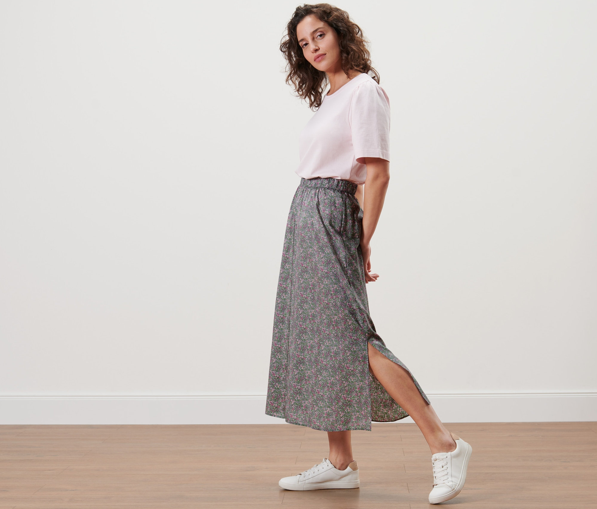 Femme posant en jupe midi florale et baskets blanches.