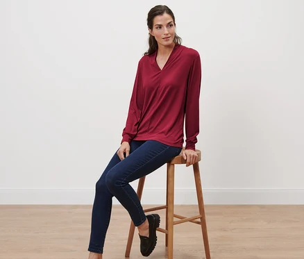 Femme assise sur un tabouret portant un t-shirt à manches longues avec encolure en V, rouge bordeaux.