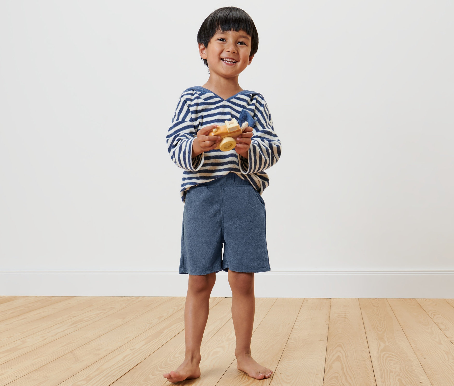 Garçon souriant tenant un avion jouet en bois et portant 2 shorts pour enfant.
