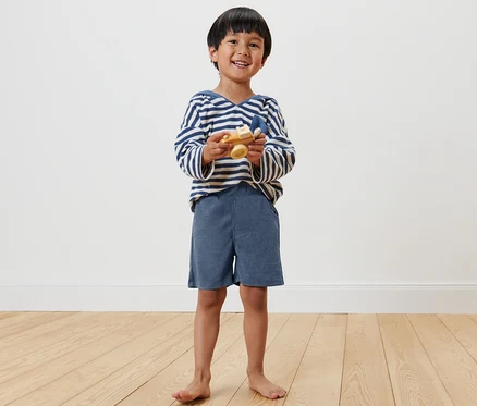 Garçon souriant tenant un avion jouet en bois et portant 2 shorts pour enfant.