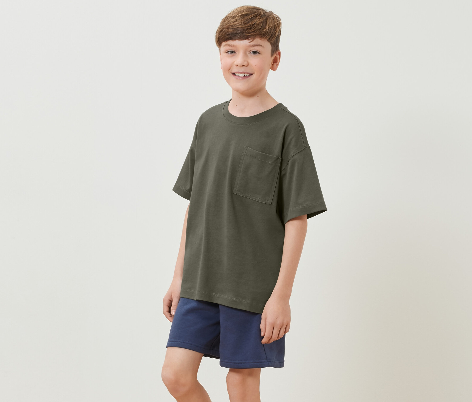 Garçon portant un t-shirt heavy pour enfant avec des épaules tombantes et un short bleu.