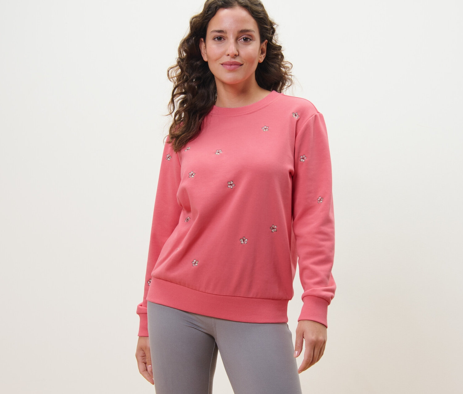 Une femme porte un sweat-shirt brodé rose et un legging gris.