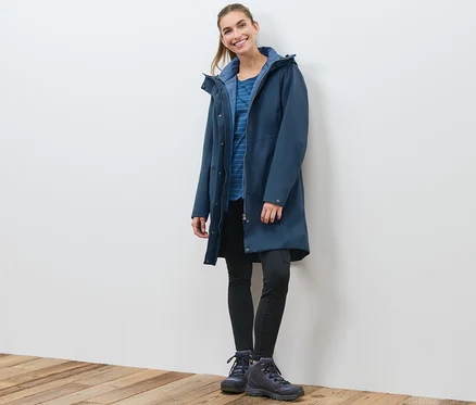 Une femme pose et porte un manteau technique 3 en 1 bleu marine avec gilet sans manches.