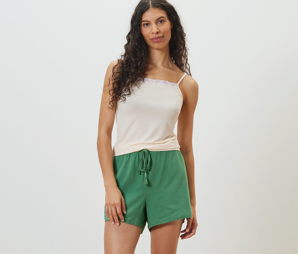 Femme posant dans un débardeur clair et un short vert.