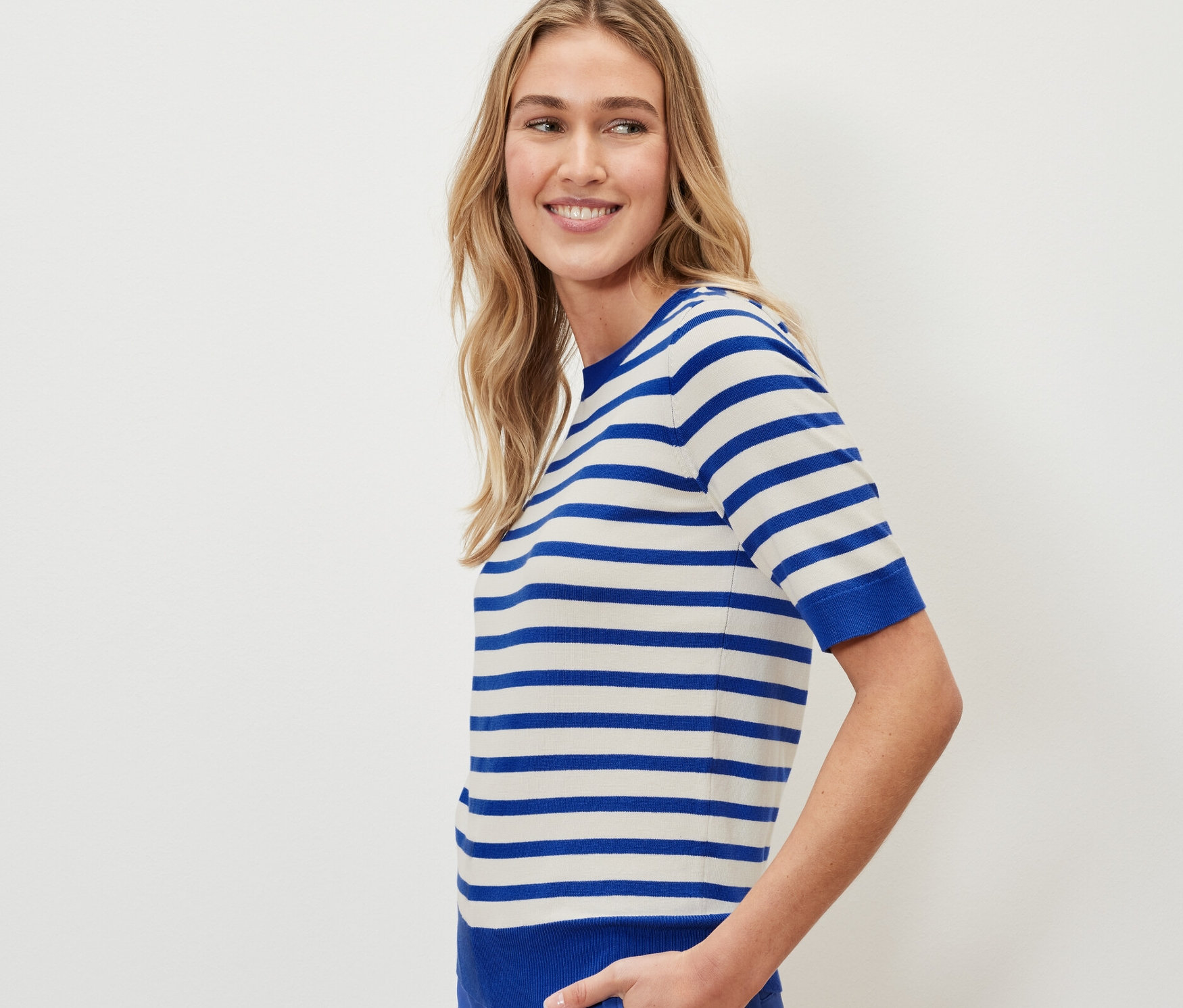 Une femme porte un pull en maille fine rayé et un pantalon bleu.