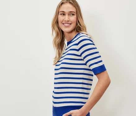 Une femme porte un pull en maille fine rayé et un pantalon bleu.