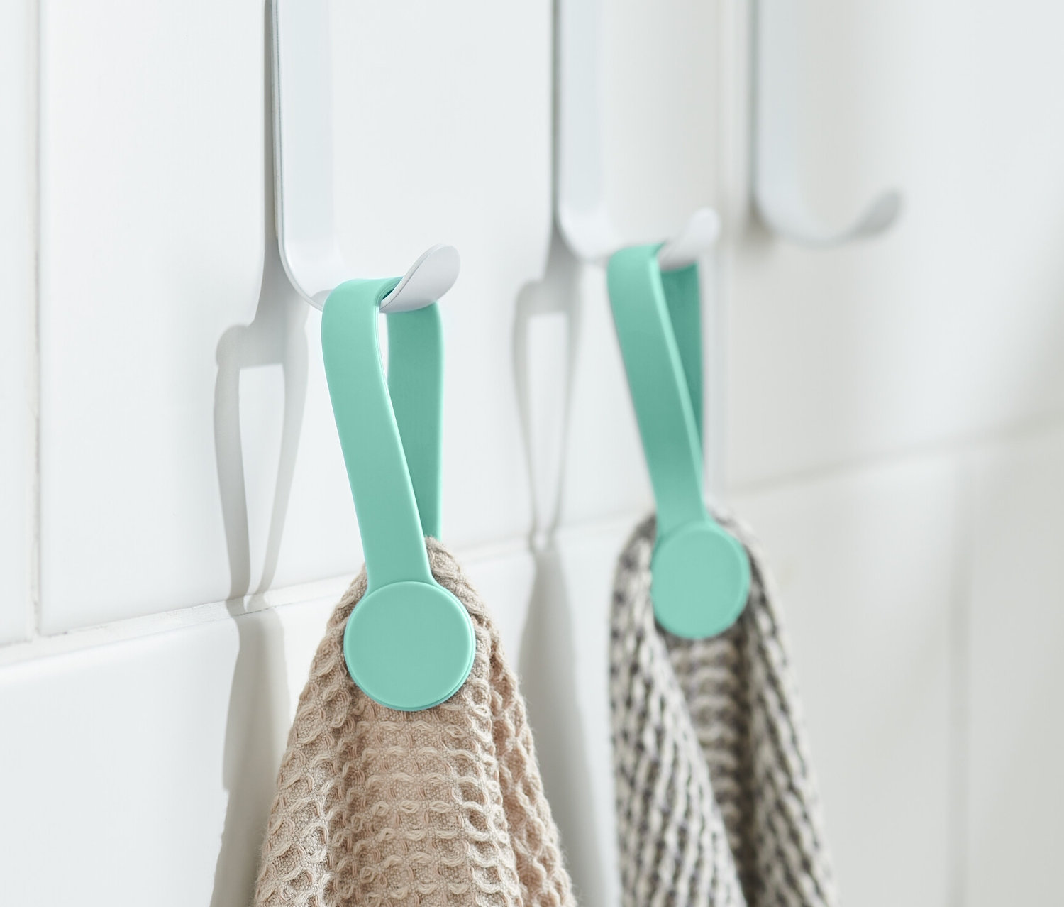 Deux clips magnétiques maintiennent des serviettes sur des crochets blancs sur le mur.