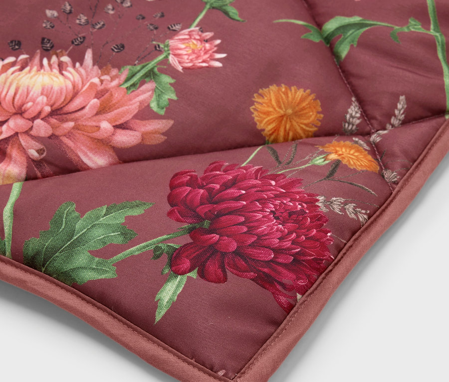 Gros plan sur le coin d'une courtepointe avec un motif floral dans les tons rouge, orange et vert.